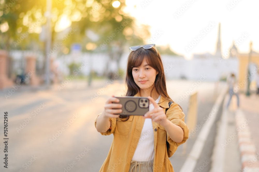 Traveler asian woman in her 30s using smartphone to take a photo while traveling urban street in Bangkok, Thailand