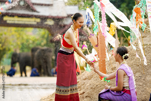 Beautiful Thai young lady ware Thai traditional dress give a small paper flags to her friends to help place in the sand in temple at the Songkran festival. © Atiwat