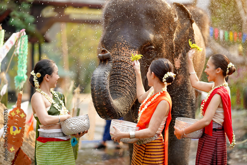 Group of Thai women ware Thai traditional dress play to sprinkle water on the Thai New Year's Day or Songkran festival in a fun way with elephant in temple on blurred background. © Atiwat
