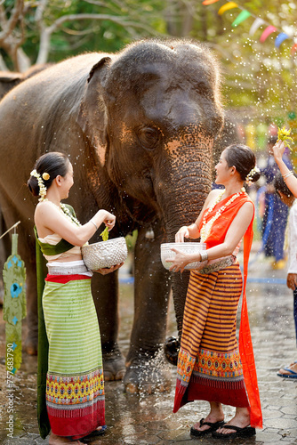 Beautiful Thai young women ware Thai traditional dress play to sprinkle water on the Thai New Year's Day or Songkran festival in a fun way with elephant on sun bright background.