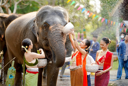 Group of Thai women ware Thai traditional dress play to splashing water on the Thai New Year's Day or Songkran festival in a fun way with elephant in temple background. © Atiwat