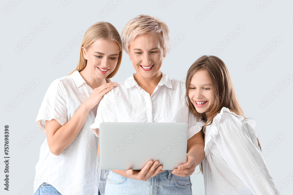 Little girl with her mom and grandmother using laptop on light background Little girl with her mom and grandmother using laptop on light background
