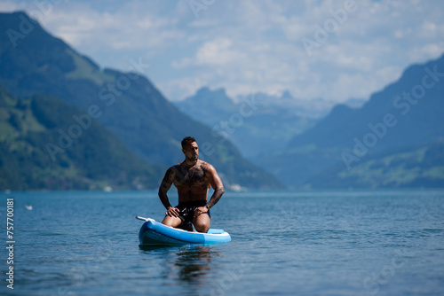 Man on paddle board in Alps lake mountains. Leisure activities with paddle on Lake in Switzerland. Man paddle surfing board on Geneva Lake. Muscular sexy strong Hispanic man paddle board surfers.