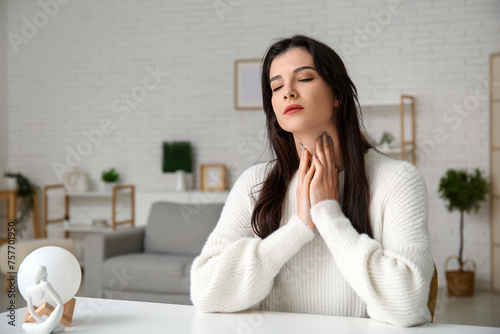 Young woman with thyroid gland problem sitting at table in living room