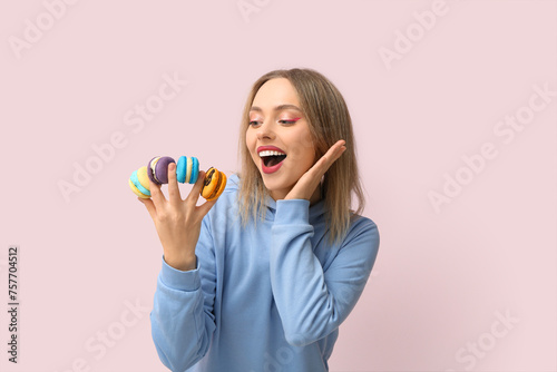 Beautiful young woman with different sweet macaroons on pink background