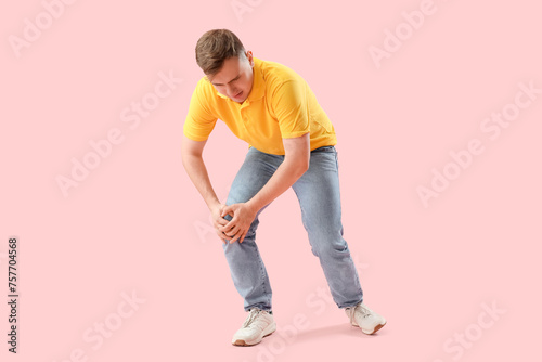 Young man suffering from knee pain on pink background
