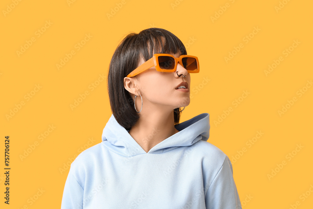 Stylish young woman in sunglasses with nose piercing on yellow background Stylish young woman in sunglasses with nose piercing on yellow background