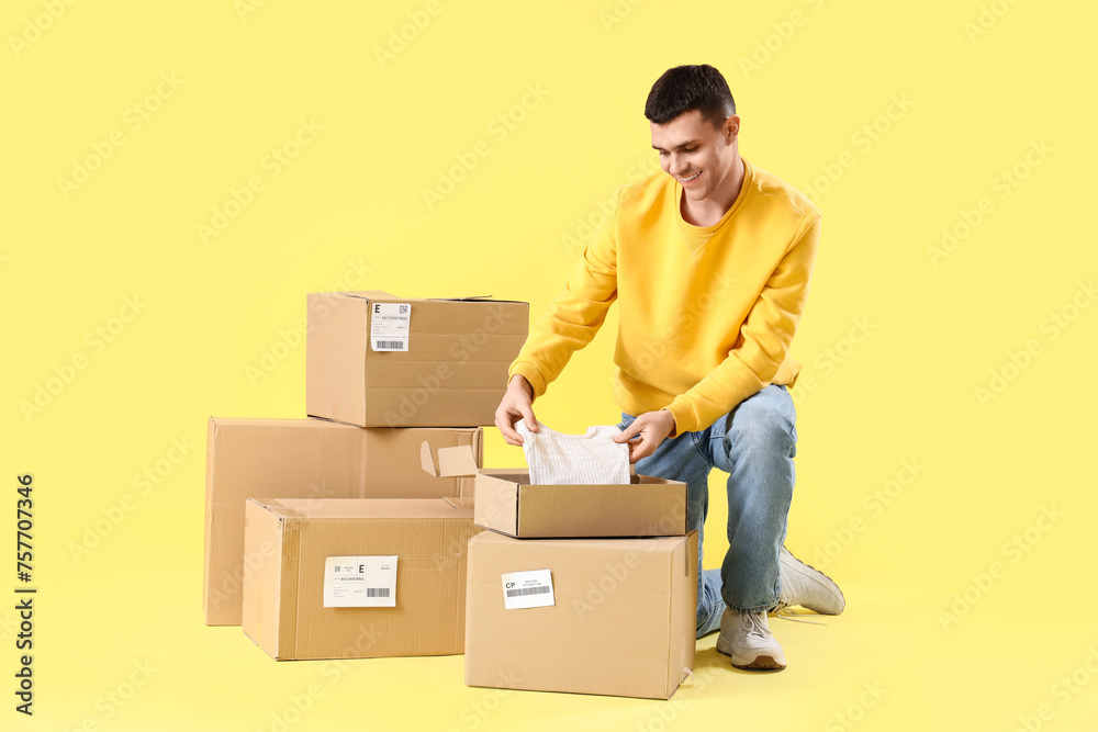 Male online store seller and parcel boxes with clothes on yellow background Male online store seller and parcel boxes with clothes on yellow background