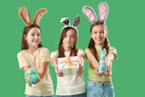 Cute little girl with Easter bunny ears, gift, egg and toy rabbit on green background