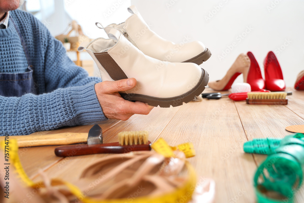 Fototapeta premium Male shoemaker with boots at table in workshop, closeup