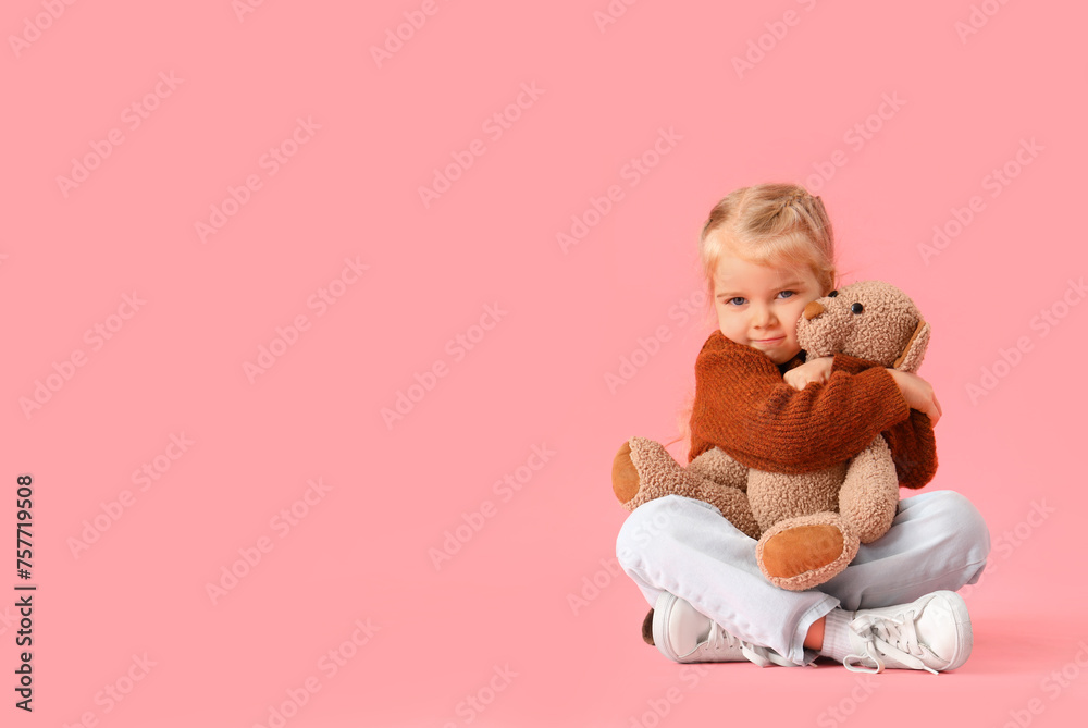 Little girl with autistic disorder hugging toy bear on pink background