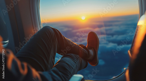 Passenger perspective of a stunning sunset viewed from an airplane window, with a focus on the relaxed feet up against the window © KaiTong