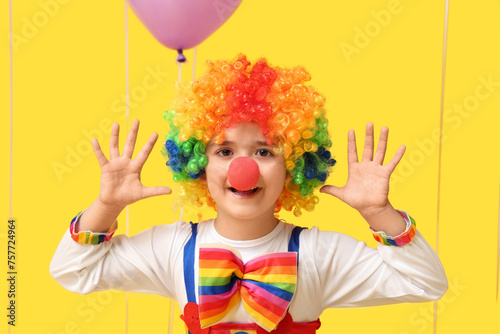 Funny little boy in clown costume on yellow background. April Fools Day celebration