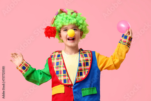 Funny little boy in clown costume with balloon on pink background. April Fools Day celebration