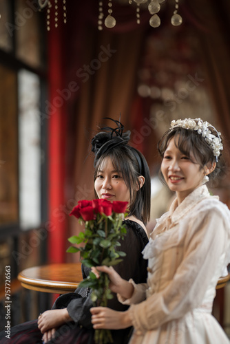 A woman in white and a woman in black look at the camera holding roses.