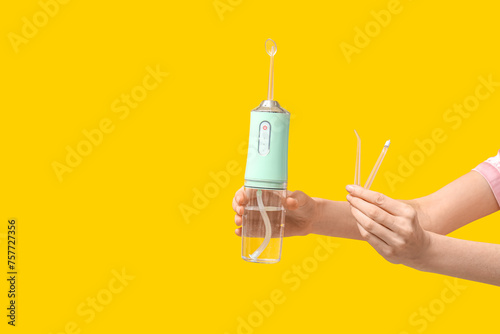 Female hands with oral irrigator on yellow background