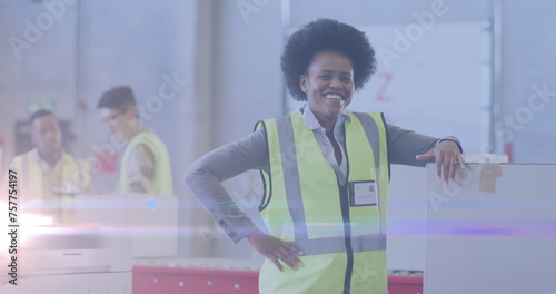 Image of glowing light over african american woman working in warehouse