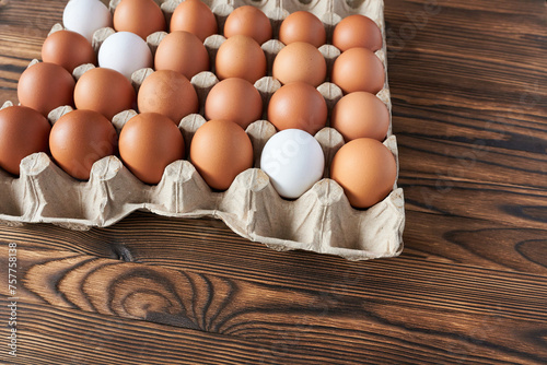 Chicken eggs in a cardboard box on a wooden background. Top view photo