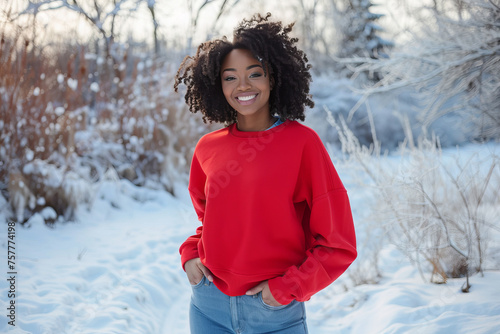 Portrait of an attractive black afro American female model wearing red blank mockup crewneck sweatshirt and posing in front of winter scene with snow