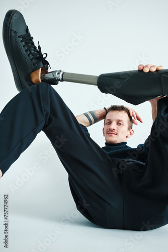 Studio portrait of a successful happy tattooed one legged disabled young male amputee with prosthetic leg wearing casual dark blue clothing. 