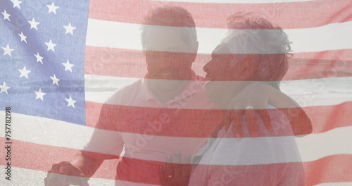 Image of flag of united states of america over senior biracial couple kissing on beach