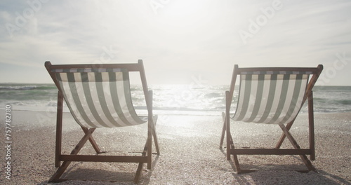 Two striped deck chairs face the ocean on a sunny beach, with copy space