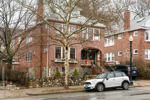 Traditional two-story red brick house surrounded by bare trees, with a parked car on the street in front, Brighton, MA, USA