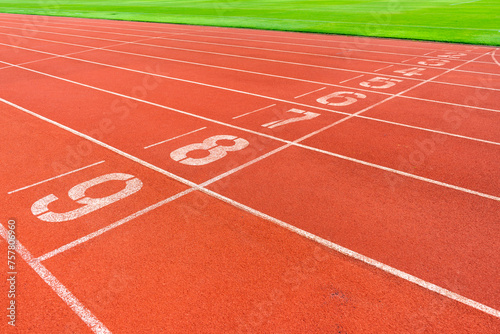 Red running track with green grass in stadium. Athletic competitions starting line positions from one to nine.