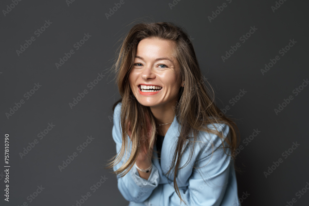 Portrait of a beaming young woman dressed in casual blue, against a grey backdrop. Portrait of a beaming young woman dressed in casual blue, against a grey backdrop.