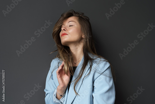A young woman in a blue jacket closes her eyes, savoring a quiet moment.