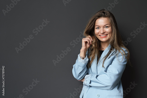 Professional woman with a charming smile wearing a blue blazer on a grey backdrop.