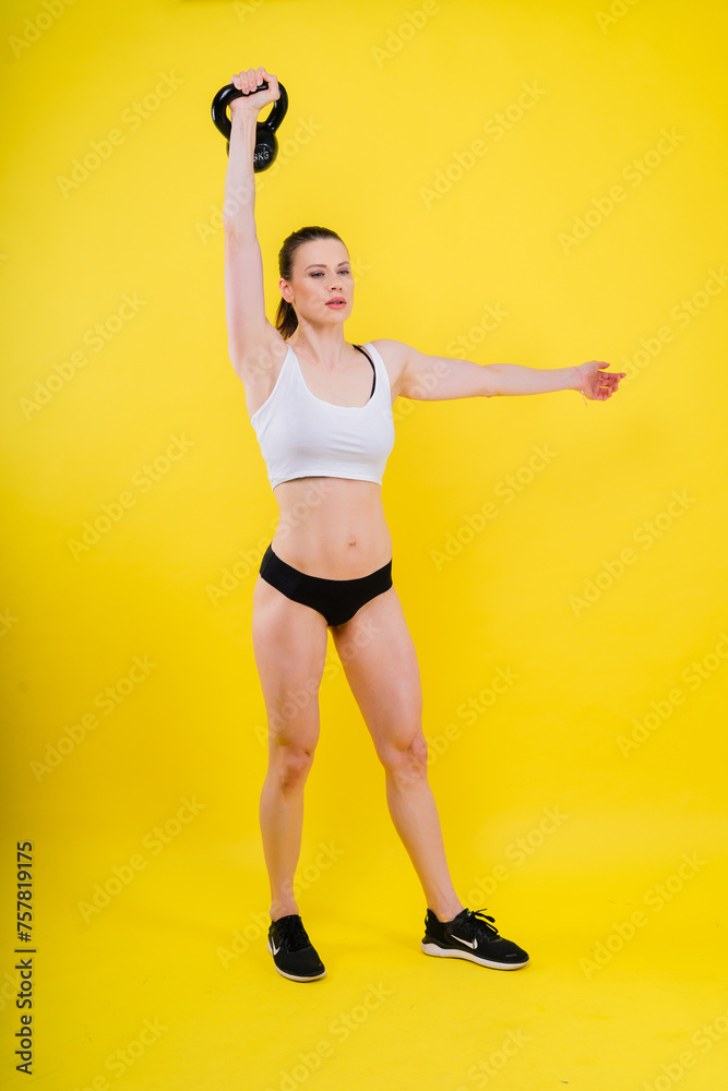 Fitness female holds a kettlebell in rack position, dark yellow red background Fitness female holds a kettlebell in rack position, dark yellow red background
