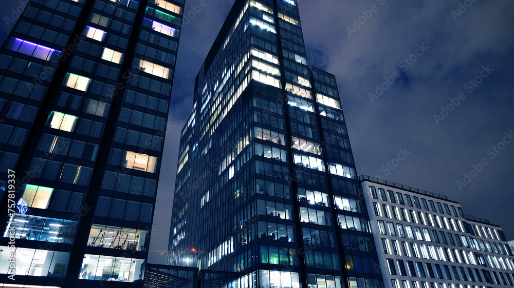 Naklejka premium Office building at night, building facade with glass and lights. View with illuminated modern skyscraper.