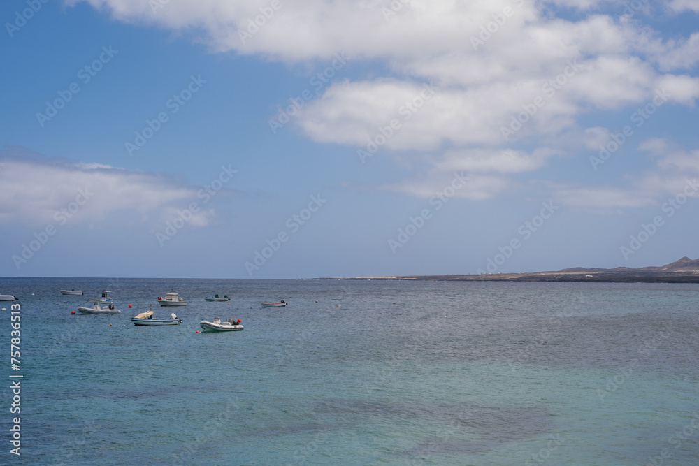Seascape. Group of boats anchored near the pier. Turquoise Atlantic Ocean. Big white clouds. Village of Arrieta. Lanzarote, Canary Islands, Spain