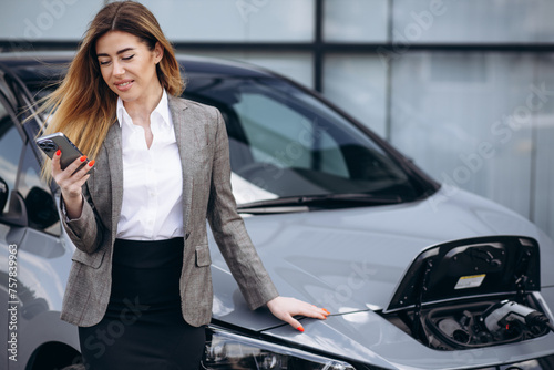 Business woman charging electric car and using mobile phone