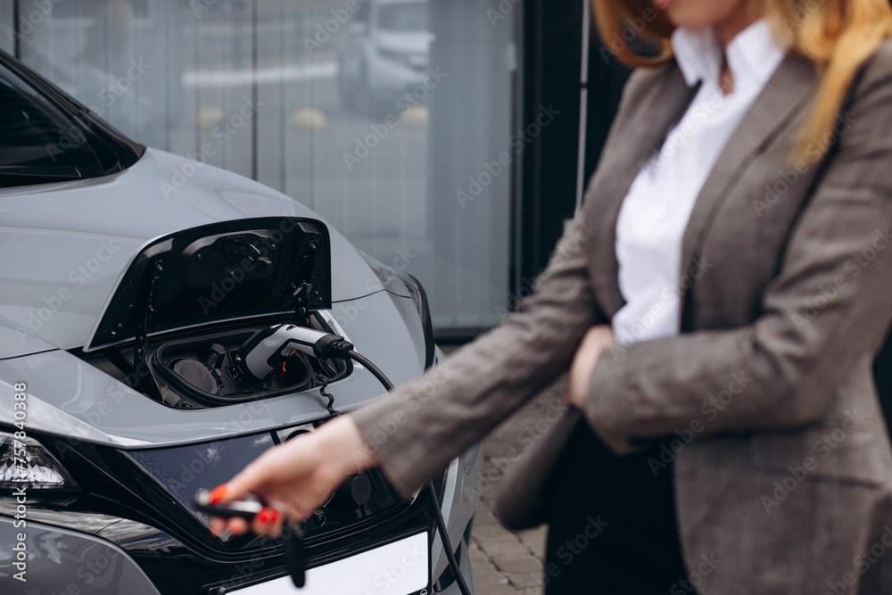 Woman holding socket and charging electric car Woman holding socket and charging electric car