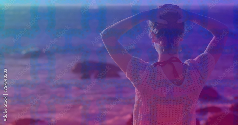 Pink square design pattern against rear view of caucasian woman standing on the rocks near the sea