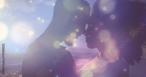 Glowing blue spots of light over african american couple embracing each other on the rocks near sea