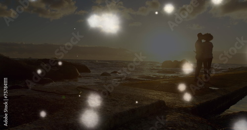 Glowing spots of light floating against african american couple standing together on the rocks
