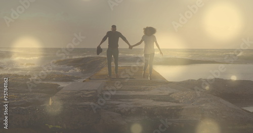 Glowing spots of light against african american couple holding hands running on the rocks