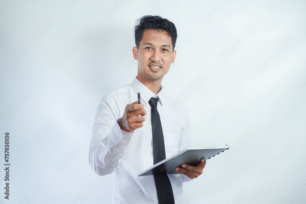 young Asian businessman holding a notebook in his hand while pointing and looking at the camera with a smile on his face. isolated on white background young Asian businessman holding a notebook in his hand while pointing and looking at the camera with a smile on his face. isolated on white background