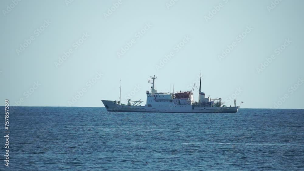Fishing boat trawler catches fish while sailing on sea. A commercial fishing boat on the horizon in a distance sail to catch school of fish on calm sea surface in summer. Commercial catch of sea fish. Fishing boat trawler catches fish while sailing on sea. A commercial fishing boat on the horizon in a distance sail to catch school of fish on calm sea surface in summer. Commercial catch of sea fish.