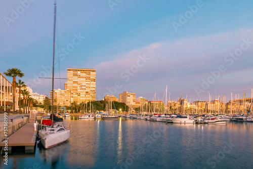 Beautiful port of Alicante at sunrise, Spain at Mediterranean sea. Luxury yachts, ships, ferries and fishing boats sailing and standing in rows in harbor. Rich people traveling around the world.