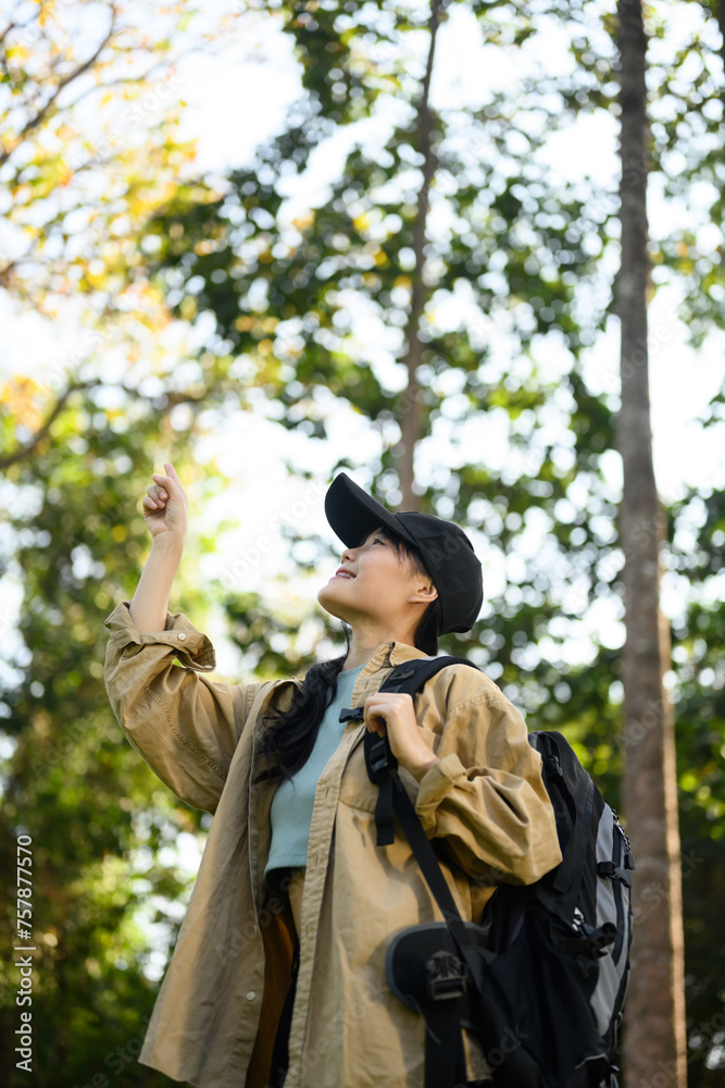 Happy young woman with backpack exploring the forest trail and admiring beauty of nature