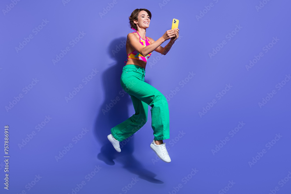 Full body length photo of young hipster funny lady jumping with smartphone holding smartphone isolated on violet color background