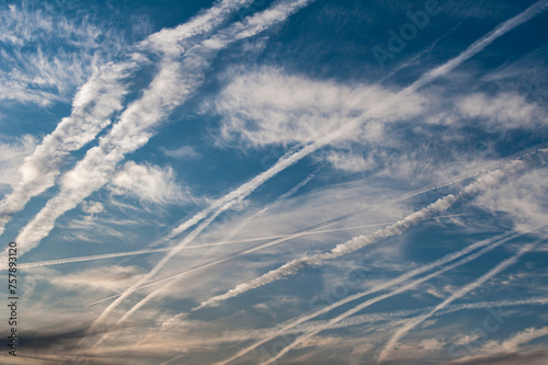Gewirr von sich teilweise auflösenden Kondensstreifen am blauen Himmel mit leichter Bewölkung und Cirruswolken