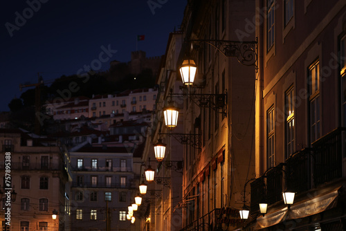 Lisbon by night. Photo with the vintage light bulbs on the street during blue hour with Lisbon Fortress Saint George in background. Travel to Portugal.