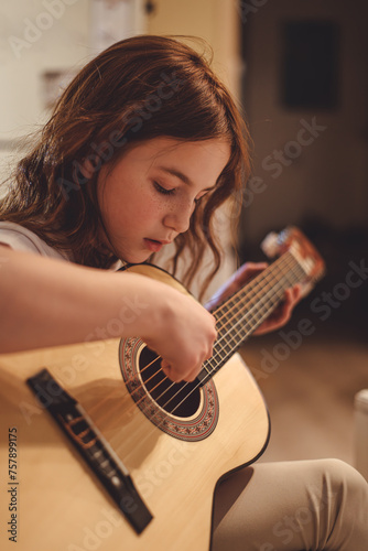 Close up of a teenage girl learning to playing acoustic guitar at home. Young girl playing music on guitar.