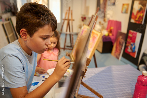 Caucasian handsome teenage school boy focused on painting on canvas in creative art workshop