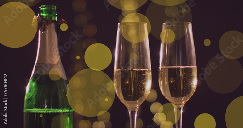 Image of yellow spots of light over two glasses and bottle of new year champagne